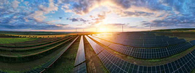 Photovoltaic power station and wind turbines at sunset panorama. Windmill turbines generating green...