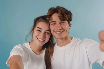 cute smiling young couple in white tshirts taking playful selfie together against blue background