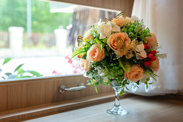 A colorful artificial roses bunch in the glass flower pot which is placed on the table for interior...