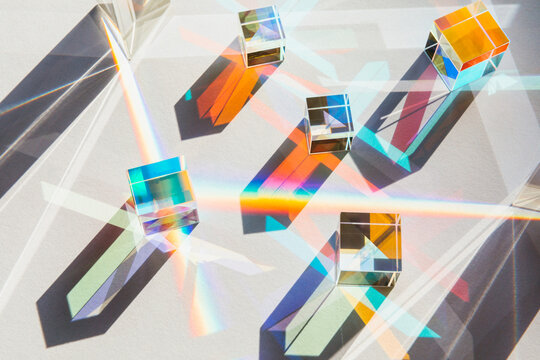 Glass geometric figures prisms with light diffraction of rainbow spectrum colors and complex reflection on white table background. Sun, trendy sunlight and shadows. Overhead view, flat lay.