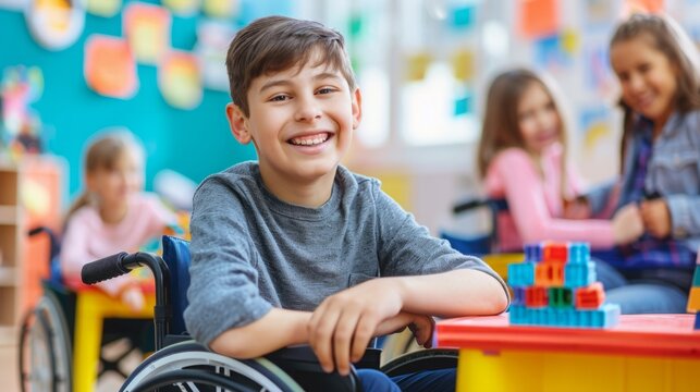 A boy in a wheelchair is smiling in front of a classroom full of students and a teacher.