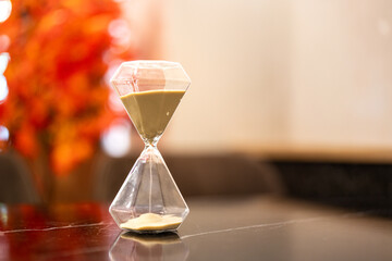 A sandglass or hourglass is placed on table. Interior decoration object photo, selective focus.