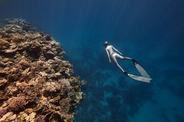 Freediver woman swim in blue ocean over coral reef