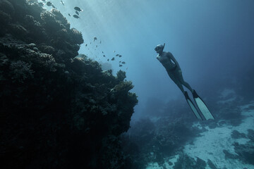 Freediver woman swim in blue ocean over coral reef