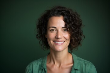 Portrait of a jovial woman in her 40s smiling at the camera in front of soft green background