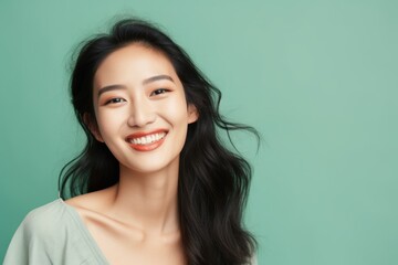 Portrait of a tender asian woman in her 20s smiling at the camera in soft green background