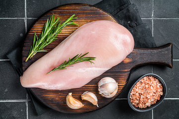Raw chicken breast fillet on a wooden board with rosemary and garlic, poultry meat. Black...