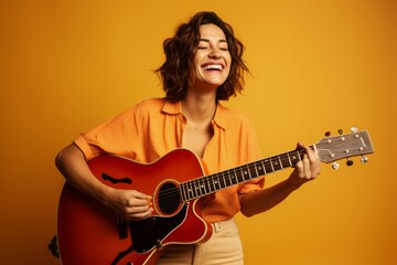 Fototapeta premium Portrait of a smiling woman in her 30s playing the guitar isolated on soft orange background