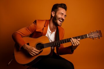 Obraz premium Portrait of a grinning man in his 30s playing the guitar in front of soft orange background