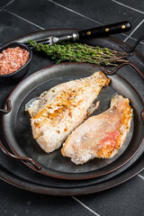 Roasted ocean red perch fillet with olive oil, thyme and spices. Black background. Top view