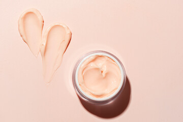 Open jar of beauty cream and swatch on pink peach background