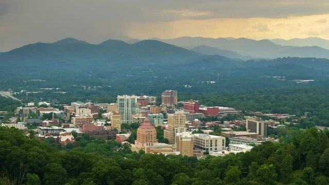 Asheville city in North Carolina with high buildings and Appalachian mountain hills in distance at sunset. US travel destination