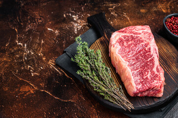 Uncooked Raw striploin or club steak on wooden board with thyme. Dark background. Top view. Copy...
