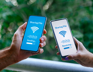 Hands of two people with mobile phones sharing files via wireless technology. Sending and receiving...