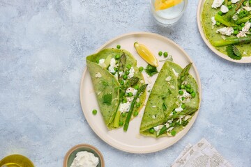 Green pancakes with spinach and nettles, stuffed with asparagus, green peas and ricotta on a ceramic plate on a gray concrete background. Seasonal products, recipes. Asparagus recipes.