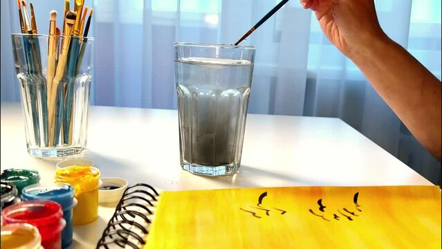 An artists is washing painting brush after drawing with watercolors. Washing brush in the water. Painting process. Side view.