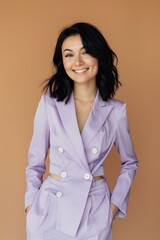 smiling woman with black hair wearing pastel purple summer suit, brown solid color background