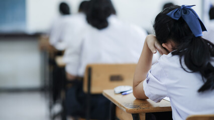 Students reading exam answer sheets exercises in classroom of school with headache.and stress