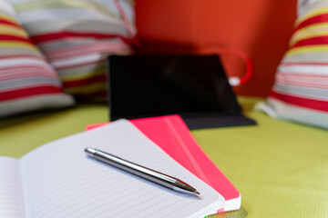 Close up of open agenda with pen on green bed and cushions in the background with tablet charging