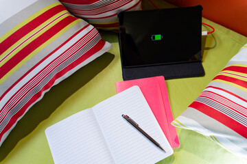 Top view of study area of young person with open agendas on white, green background colorful cushions and tablet loading