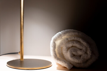 Close up of copper lamp foot illuminating small area on hotel room table with rolled towel