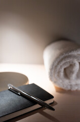 Close up of small hotel room table with lamp illuminating agenda with pen on top and rolled towel