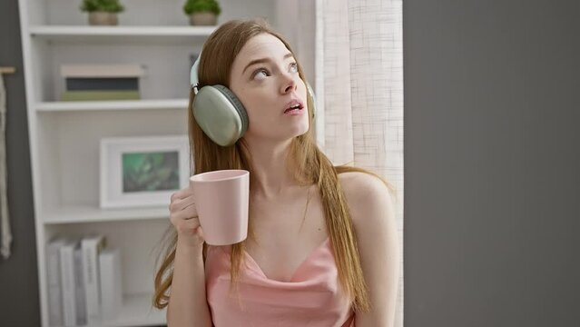 A relaxed young woman in a bedroom enjoying music through headphones while holding a coffee cup.