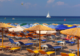 Colorful beach scene in Rhodes, Greece, with loungers and sailing boat