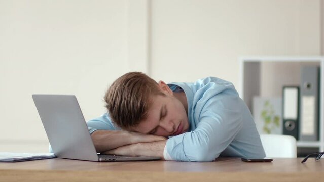 Tired young man sleeping on laptop at workplace table, working from home