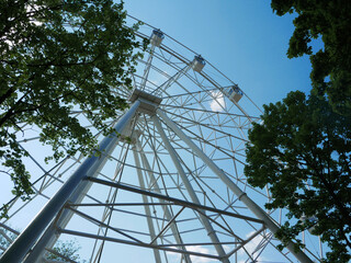 Ferris wheel against the background of blue sky and trees.