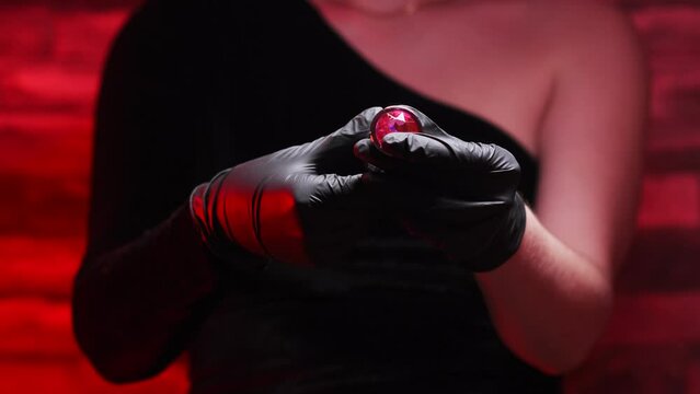 Metal anal plug in female hands in black latex gloves and a black dress on a red background. Sex shop, Adult store. BDSM - outfit for sex games for adults

