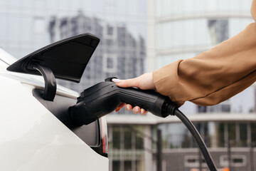 Close-up female hands unplug charger plug from charging station to his electric car before driving...