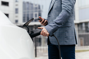 Businessman plugging electric car from charging station. Senior is plugging in power cord to an electric car. Charging electric car at charging station.
