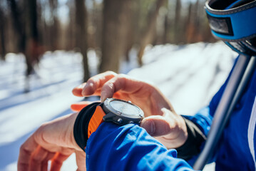 Close-up of a skier's hand adjusting a smartwatch in the snowy woods, a tool for monitoring time...