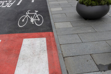 A bicycle symbol on a gray pavement next to a red and white striped area, with a black planter...