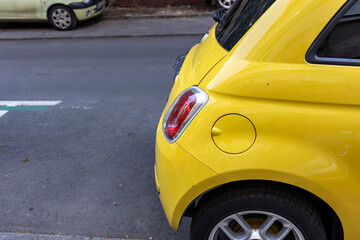 A vibrant yellow hatchback with a rear spoiler and antenna is parked in an urban parking lot, with...