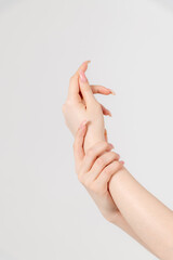 Close-up view of caucasian woman rubbing her wrist using other hand against grey background. Soft focus. Healthcare, cosmetics and self massage theme.