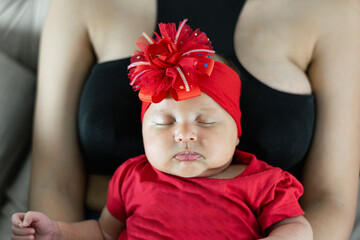 close-up of the face of a beautiful newborn latina baby sleeping on her mother's chest, dressed in...