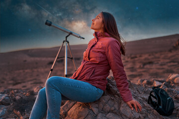 beautiful woman sitting in the desert alone next to a telescope at night watching the starry sky,...