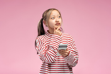 Pensive Asian girl with mobile phone holding hand near face, looking to the side, isolated