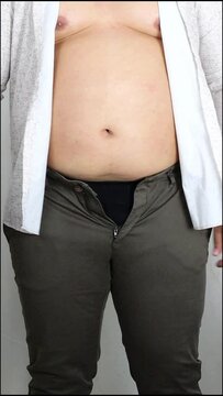 unrecognizable Male, overweight. fat man with bare fat belly shakes folds on stomach. no face. Obese man shake, spat and rub belly fat belly. Abdomen muscles jiggle. side view. isolated on white wall 