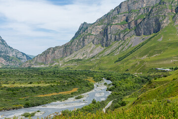 Mountain river of the village of Dargavs. Beautiful panorama of green alpine meadows, hills and...