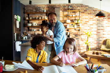 Multiracial children studying and playing with father in kitchen