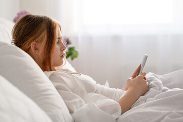 Teenage girl with mobile phone laying in bed, rest and leisure pastime, bad habits, youth gadget...