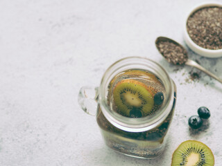View from above chia water in mason jar with kiwi and blueberry on gray cement background. Chia infused detox water with berries. Copy space for text. Healthy eating, drinks, diet, detox concept