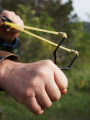 A man pulls the rubber band of a slingshot for a shot in the forest