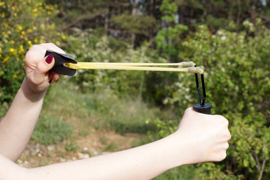A girl pulls the rubber band of a slingshot for a shot in the forest