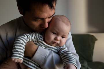 portrait of a young dad hugging and kissing his newborn baby while lying on the bed in the bedroom