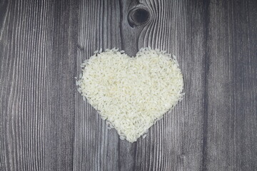 Heart-shaped rice on dark background. Love and valentines day concept. Raw long white rice in shape of heart. Traditional Asian food.
