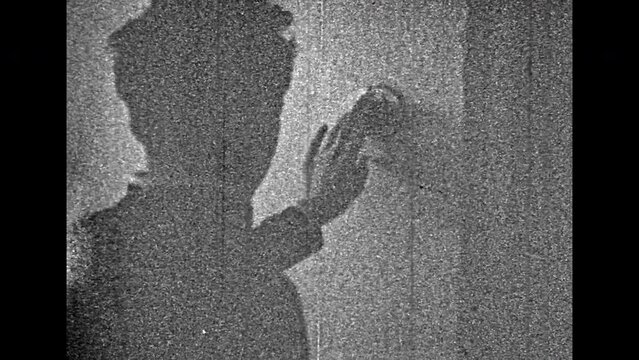 Man ringing doorbell near home entrance, back view. Vintage black white film. Male silhouette pressing house bell. Grainy film home movies of old eighties lifestyle. Family archive. Retro 1980s